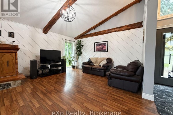 Living room with a sloped ceiling, exposed wooden beams, shiplap accent wall, fireplace, and leather sofas. - 191 5b Side Road, South Bruce