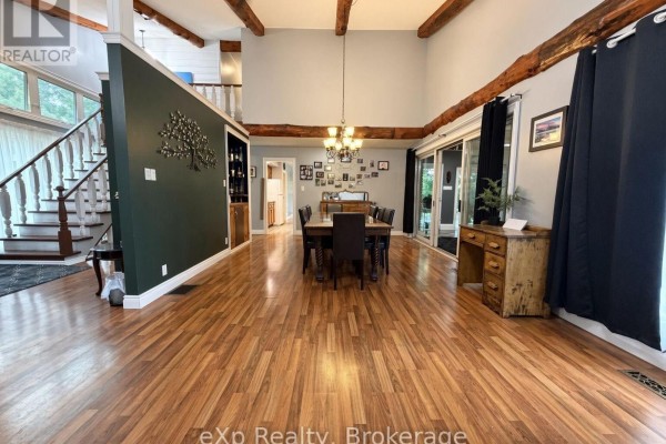 Open-concept dining and living area with wood floors, a large dining table, exposed beams, and sliding glass doors. - 191 5b Side Road, South Bruce