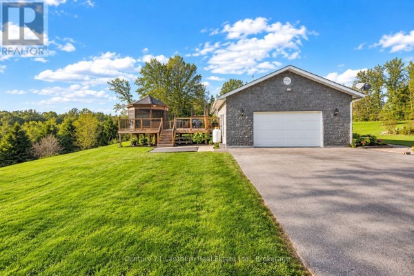 Exterior view of a stone-clad house with a garage, brick pathway, and garden beds. - 191 Emerson Road, Centre Hastings