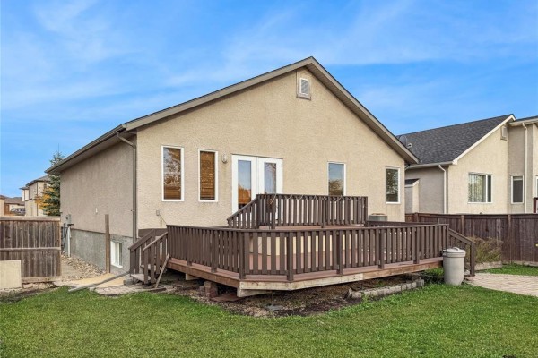 Rear exterior of the house showing a large wooden deck and a fenced backyard. - 191 Kingfisher Crescent, Winnipeg