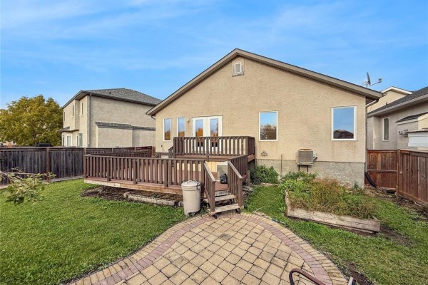 View of the backyard deck and surrounding lawn from a stone patio. - 191 Kingfisher Crescent, Winnipeg