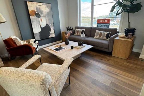 Living room with a grey sofa, accent chairs, and large window overlooking the street. - 191 Lanark Gate Se, Airdrie