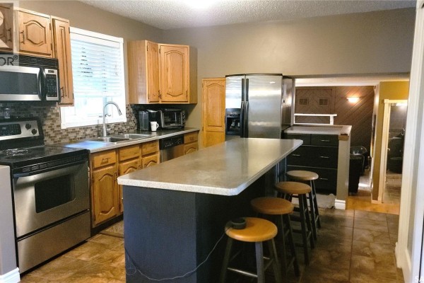 Kitchen with light oak cabinets, stainless steel appliances, and a dark island with stools. - 191 Neatby Place, Saskatoon