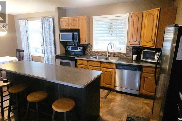 Kitchen featuring light oak cabinets, stainless steel appliances, and a dark island with stools. - 191 Neatby Place, Saskatoon