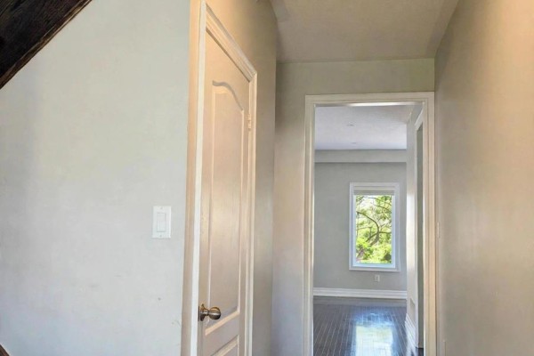Hallway view showing a closed white door and an open doorway leading to a room with a window. - 191 Reeves Way Boulevard, Whitchurch Stouffville