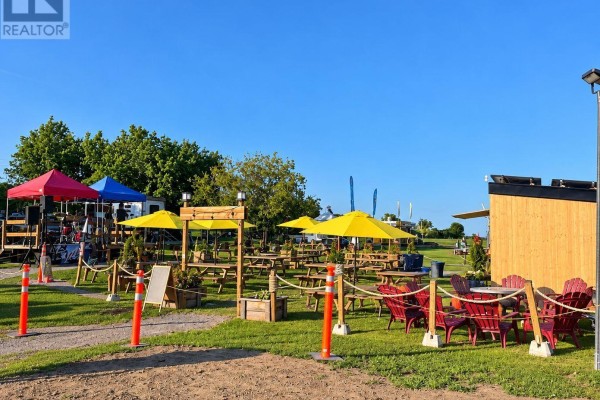 Outdoor seating area with picnic tables, red chairs, and yellow umbrellas under a blue sky. - 191 Water Street E, Prescott