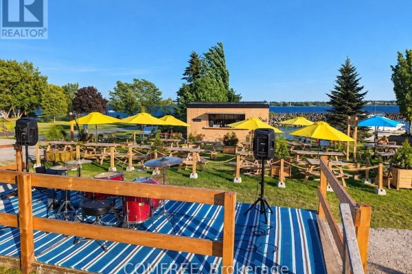 Outdoor stage with drum set and speakers set up in a grassy area with water view. - 191 Water Street E, Prescott