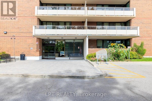 Front entrance of a brick apartment building with a paved walkway and landscaping. - 1910 - 15 Torrance Road, Toronto