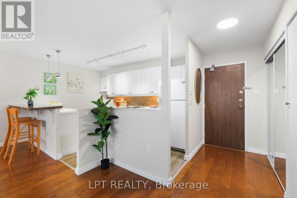 View of the kitchen, entryway, and hallway with wood floors and mirrored closet doors. - 1910 - 15 Torrance Road, Toronto