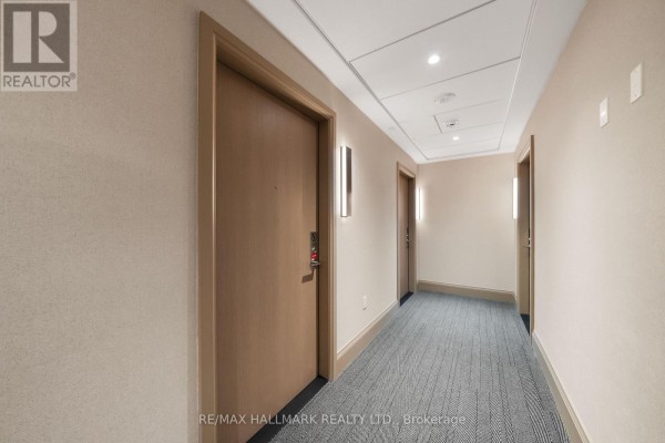 Interior hallway of an apartment building with beige carpet, beige walls, and wood doors with modern sconces. - 1910 - 21 Meadowdale Road, Vaughan