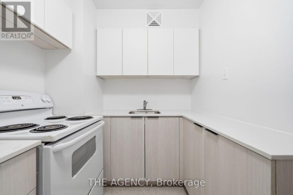 Compact kitchen with white stove, white upper cabinets, and light wood lower cabinets. - 1910a - 2350 Dundas Street W, Toronto
