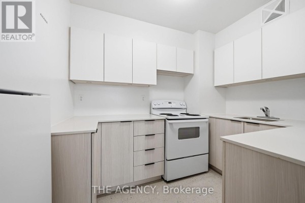 Galley kitchen with white stove, white upper cabinets, and light wood lower cabinets and counter. - 1910a - 2350 Dundas Street W, Toronto