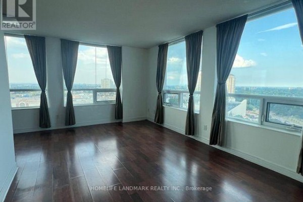 Empty living room with dark wood floors, large windows, and brown curtains. - 1912 - 83 Borough Drive, Toronto
