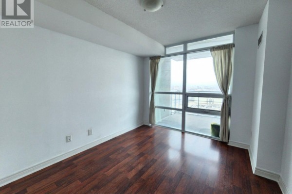 Empty bedroom with dark wood floors and a large window overlooking the city. - 1912 - 83 Borough Drive, Toronto