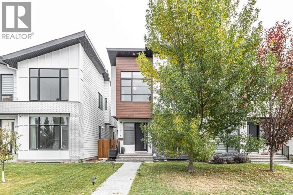 Side view of a modern duplex with white brick and wood accents, flanked by trees. - 1912 23 Avenue Nw, Calgary