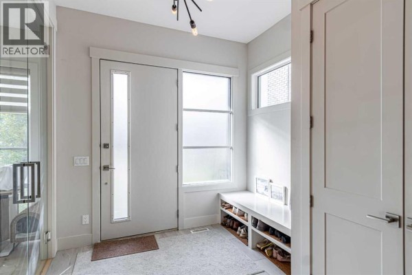 Bright entryway with a frosted glass door, white bench with shoe storage, and light grey walls. - 1912 23 Avenue Nw, Calgary