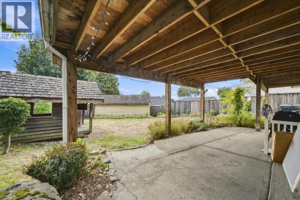 Covered patio area with concrete floor and wooden support beams, overlooking a backyard. - 1912 London Street, New Westminster