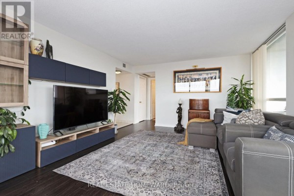 Living room featuring a large television, entertainment unit, and grey sectional sofa. - 1913 - 4725 Sheppard Avenue E, Toronto