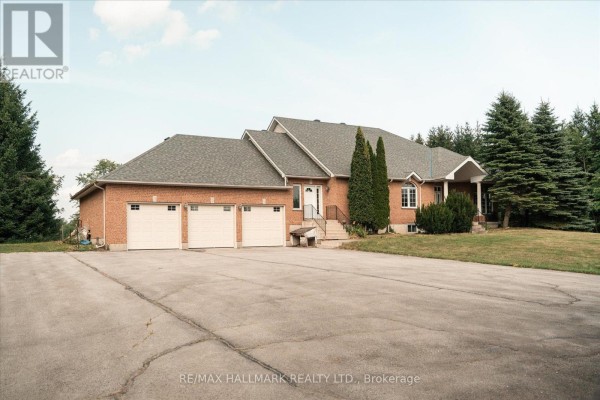 Side view of a large brick house with a dark roof, showing three of the six garage doors. - 191555 13 Line, East Garafraxa