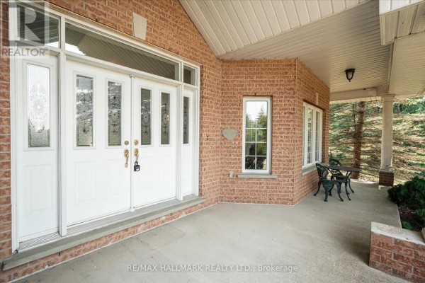 Covered front porch with brick walls, white columns, and a table with two chairs. - 191555 13 Line, East Garafraxa
