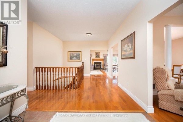 Interior hallway with hardwood floors, staircase, fireplace, and dining area visible in background. - 191555 13 Line, East Garafraxa