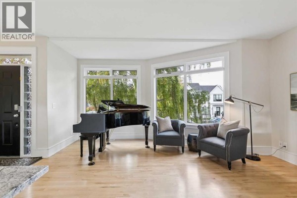 Living room with a grand piano, two armchairs, and large bay windows. - 1917 27 Avenue Sw, Calgary
