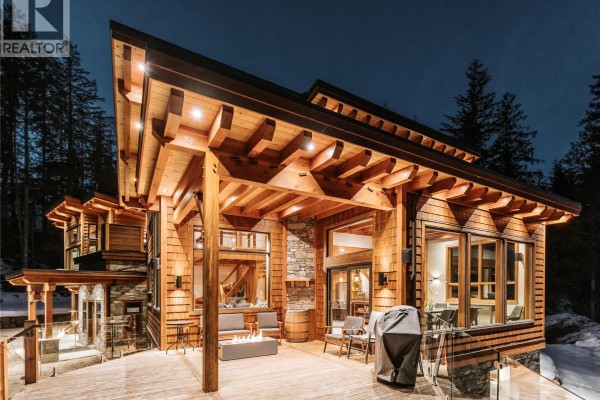 Covered outdoor living space with fireplace and seating area on a timber deck at night. - 1917 Mt Mcpherson Drive, Revelstoke