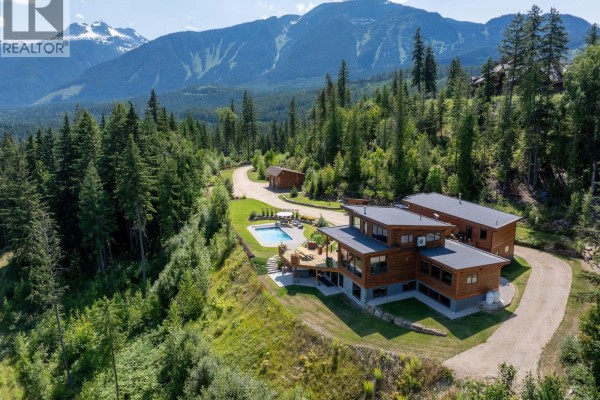 Sprawling aerial view of a multi-building property with a pool, set against a backdrop of lush green mountains. - 1917 Mt Mcpherson Drive, Revelstoke