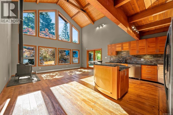 Open concept living and kitchen area with wood floors, vaulted ceiling, large windows, and modern appliances. - 1918 Chelsea Rd, Courtenay
