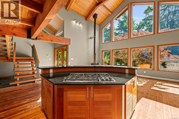 Interior view of a kitchen island with a gas range, surrounded by wood cabinetry and vaulted wooden beams. - 1918 Chelsea Rd, Courtenay
