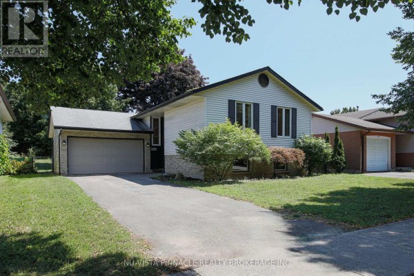 View of the residential street showing a beige house with a dark roof and attached single-car garage. - 192 Concord Road, London North
