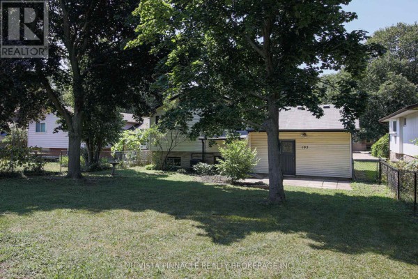 Backyard view of a single-story house with a patio area and mature trees providing shade. - 192 Concord Road, London North