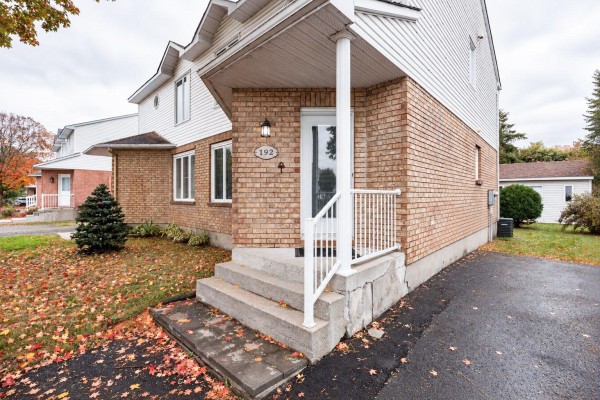 Close-up of the entrance to a beige brick house with a white door and railing. - 192 Rue De Châteaufort, Gatineau