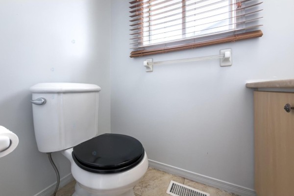 Powder room with a white toilet, black seat, and a window with wooden blinds. - 192 Rue De Châteaufort, Gatineau