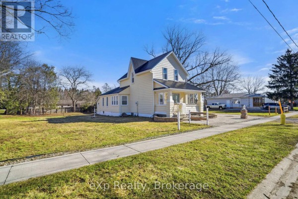 Yellow house with black metal roof, front porch, and paved driveway - 192 William Street W North Middlesex