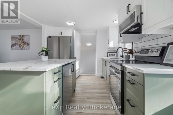 Sage green kitchen cabinets with white quartz island and subway tile backsplash - 192 William Street W North Middlesex