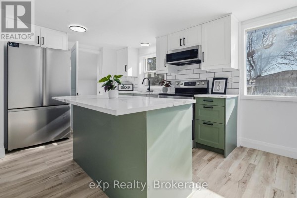 Modern kitchen with island, stainless steel fridge, and green island - 192 William Street W North Middlesex