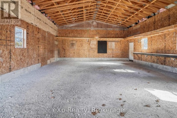 Unfinished garage with gravel floor, OSB walls, exposed beams, and workbench - 192 William Street W North Middlesex