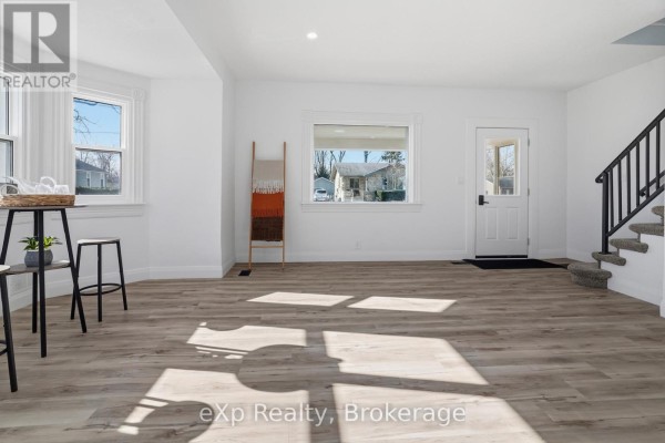 Living room with light wood floors, white walls, decorative ladder, front door, and stairs - 192 William Street W North Middlesex