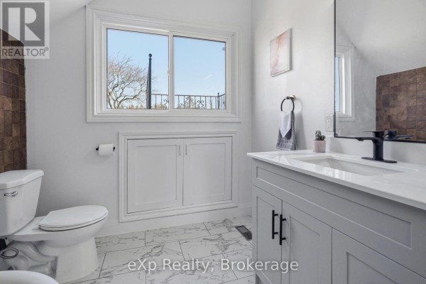 Modern bathroom vanity with black faucet, toilet, and window - 192 William Street W North Middlesex