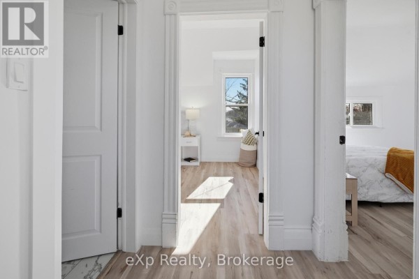 Hallway view of bedrooms with wood-look flooring and white trim - 192 William Street W North Middlesex