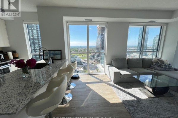 Open concept living area with large windows, grey sofa, and kitchen island. - 1920 - 4055 Parkside Village Drive, Mississauga