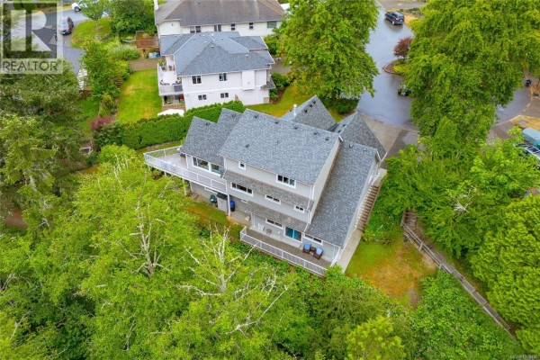 Living room with teal sofa, large windows, fireplace, and wood floors overlooking greenery. - 1927 Riverside Dr, View Royal