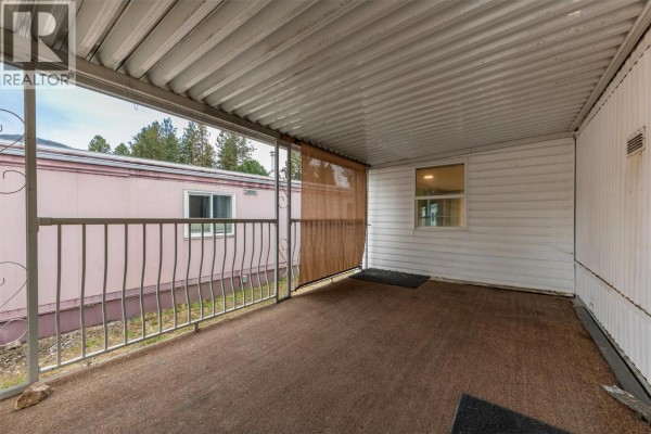 View from a covered patio showing the exterior of a pink mobile home and metal railings. - 1929 97 Highway S Unit# 45, West Kelowna