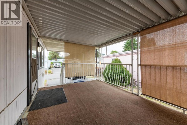 Covered patio with brown carpeting, metal railings, and sunshade screens on the exterior of a mobile home. - 1929 97 Highway S Unit# 45, West Kelowna