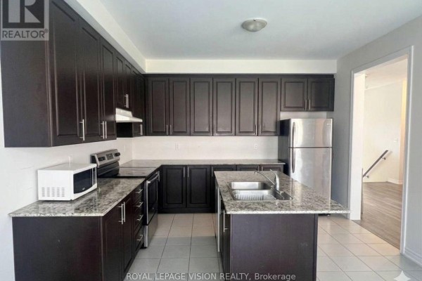 Kitchen with dark brown cabinets, granite countertops, stainless steel appliances, and an island. - 1929 Don White Court, Oshawa
