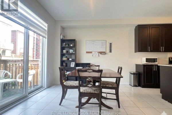 Dining area with a wooden table and chairs, dark brown cabinets, and sliding glass doors to a deck. - 1929 Don White Court, Oshawa