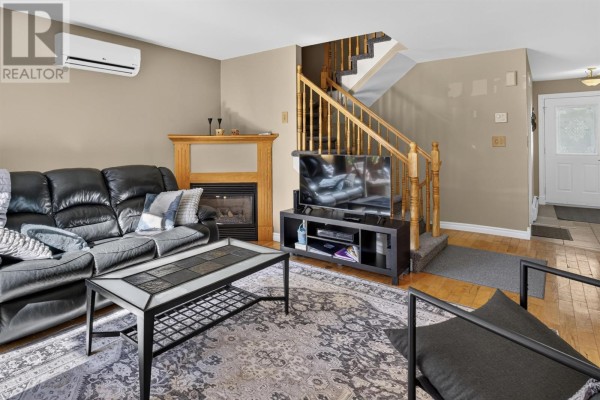 Living room with a black sectional sofa, fireplace, television, and wooden staircase. - 193-195 Hillsborough Street, Charlottetown