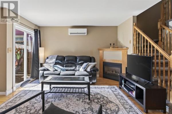 Living room facing the fireplace, with a black sofa, television, and sliding glass door. - 193-195 Hillsborough Street, Charlottetown