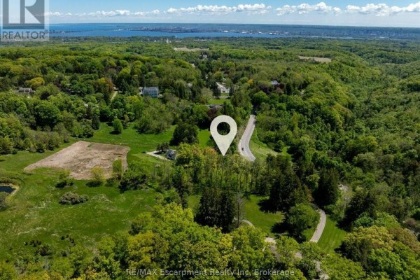 Drone view of a rural landscape with houses and distant city skyline, featuring a location pin. - 193 Mill Street S, Hamilton